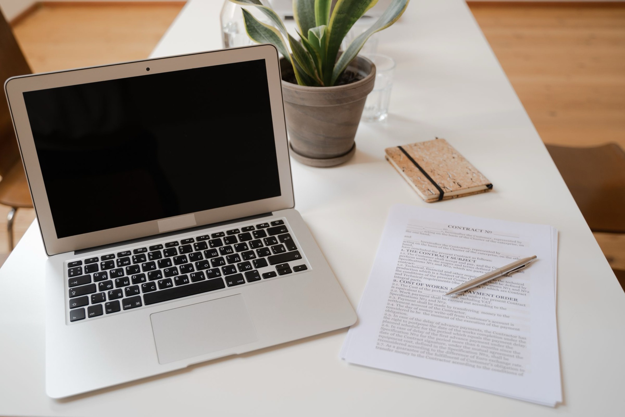 A laptop and a printed agreement on a desk.