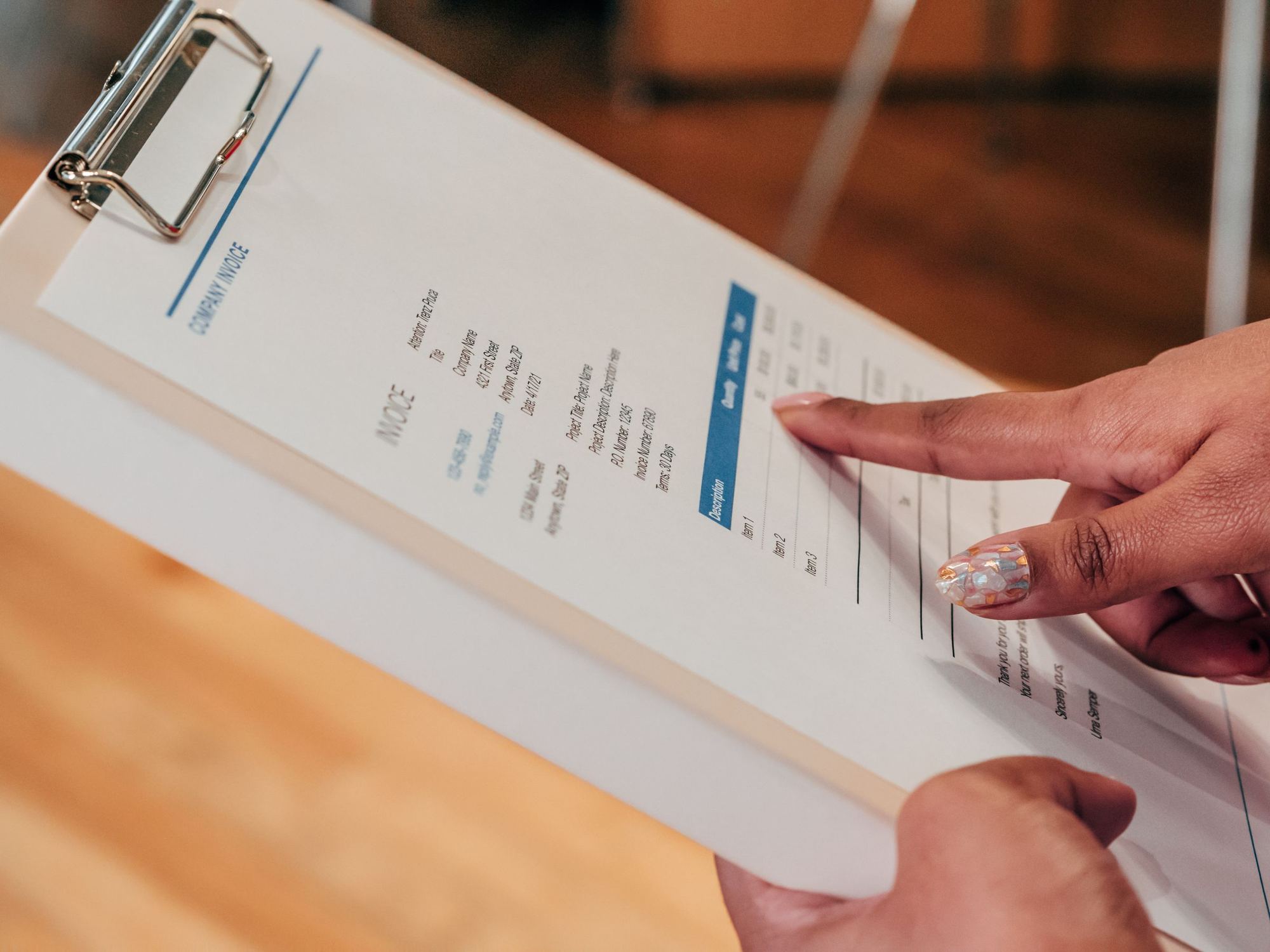 A finger pointing at a line on an invoice held on a clipboard.