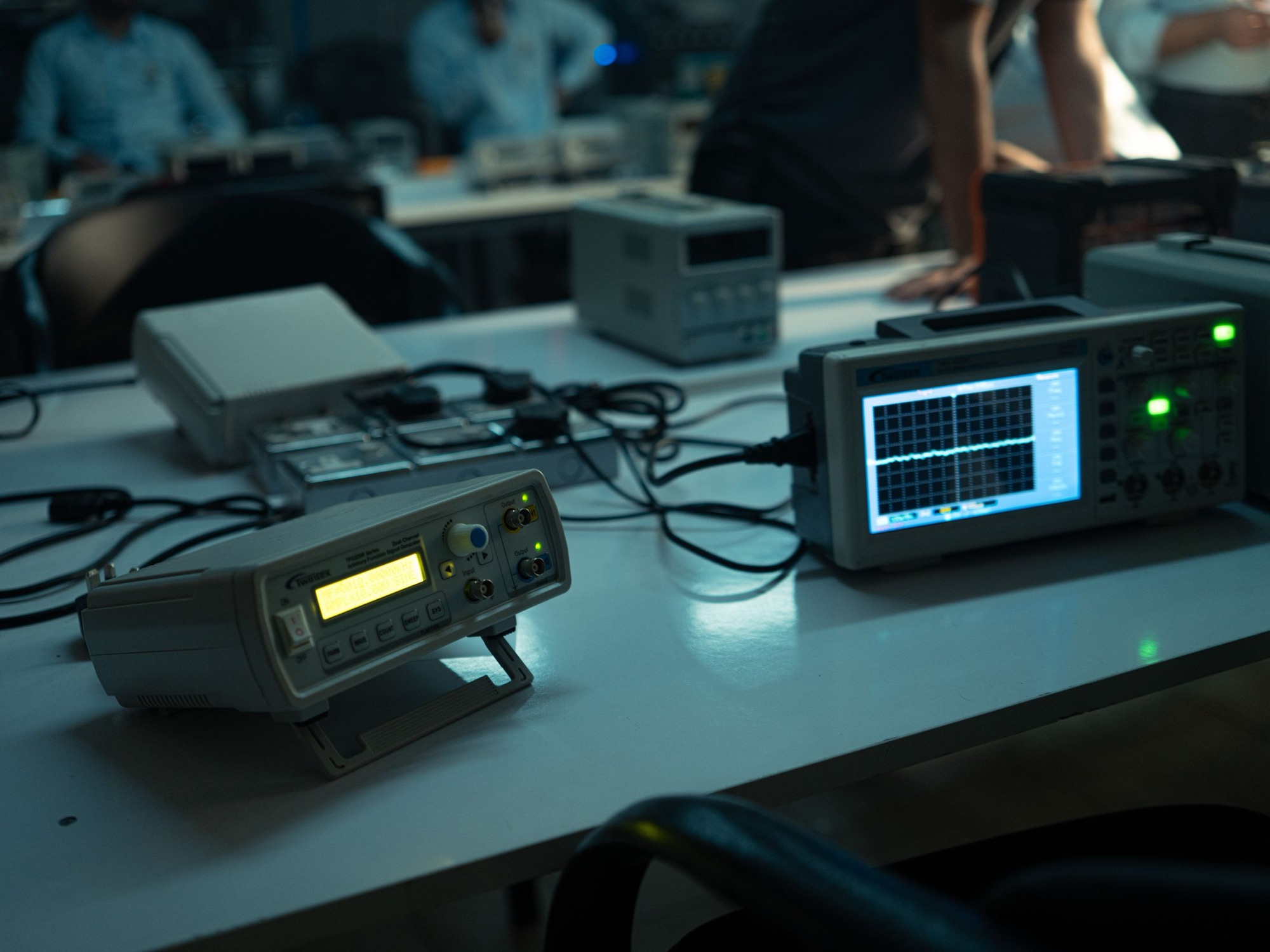 A dim electronics lab bench with an oscilloscope and a signal generator. Illustrative photograph.