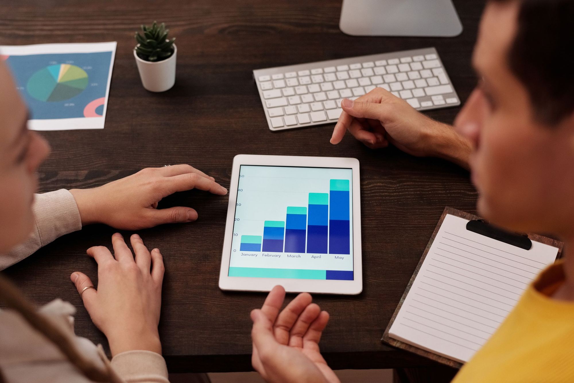 Two people reviewing a rising bar chart on a tablet.