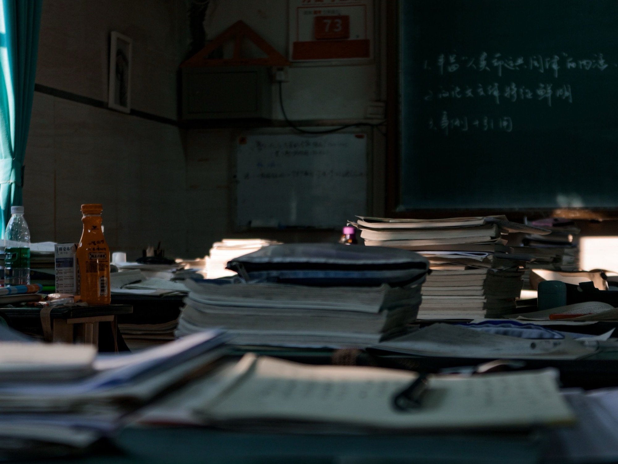 Stacks of paper and notebooks on a desk in a dim office.